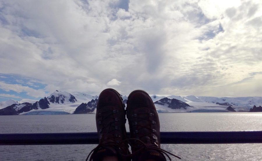 Hicks, Hoodlums, & Highrises author, Nicole Braun's hiking boots on the railing of a ship looking out at Antarctica
