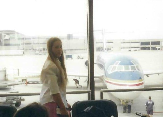 Hicks, Hoodlums, & Highrises author, Nicole Braun, as a teenager in front of an airport window overlooking a Midwest Airlines plane