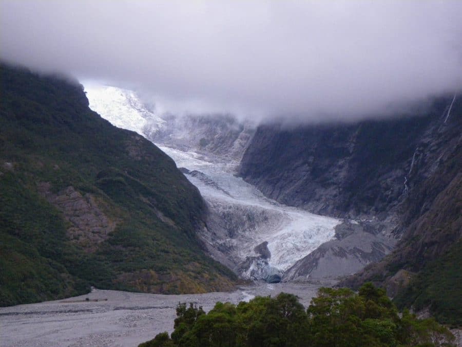 The base of Franz Josef Glacier peaks through beneath low hanging clouds