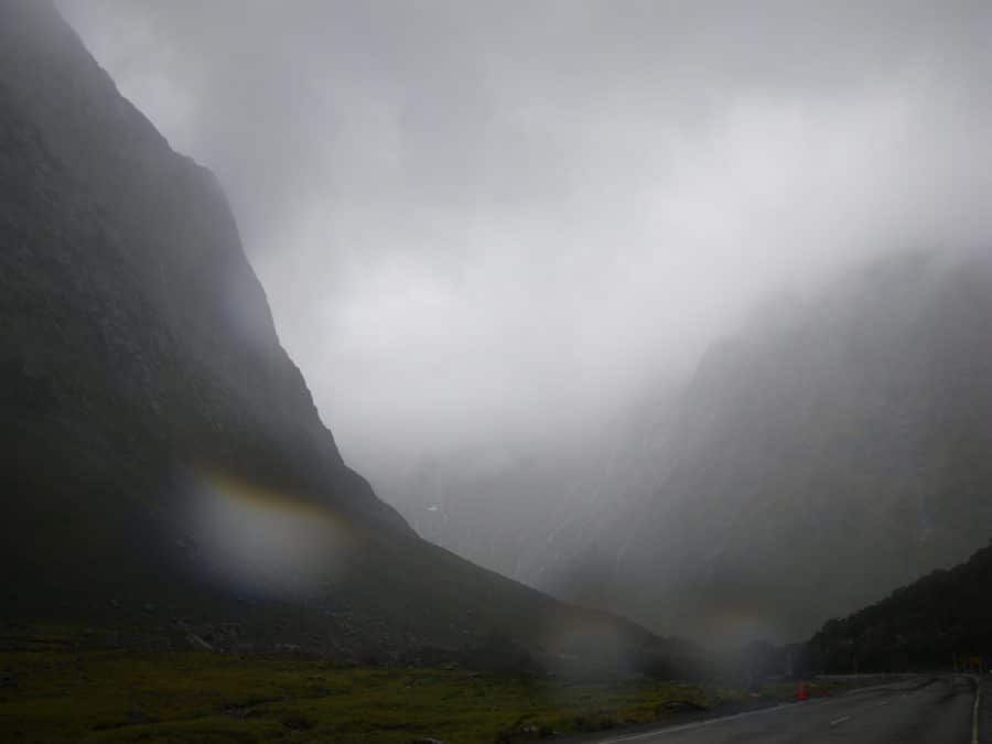 Road cutting through mountains in a rainy, brown, haze in Fiordland, New Zealand